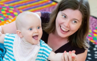 Woman and baby in arms sitting on the floor on a checked carpet.