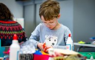 A young boy wearing glasses and a blue jumper with a white polar bear on it, works on a craft project.