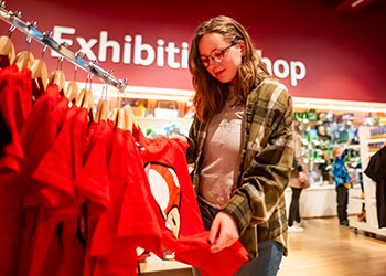 An adult looking at a rack of red t-shirts in the Game On exhibition shop at the National Museum of Scotland.