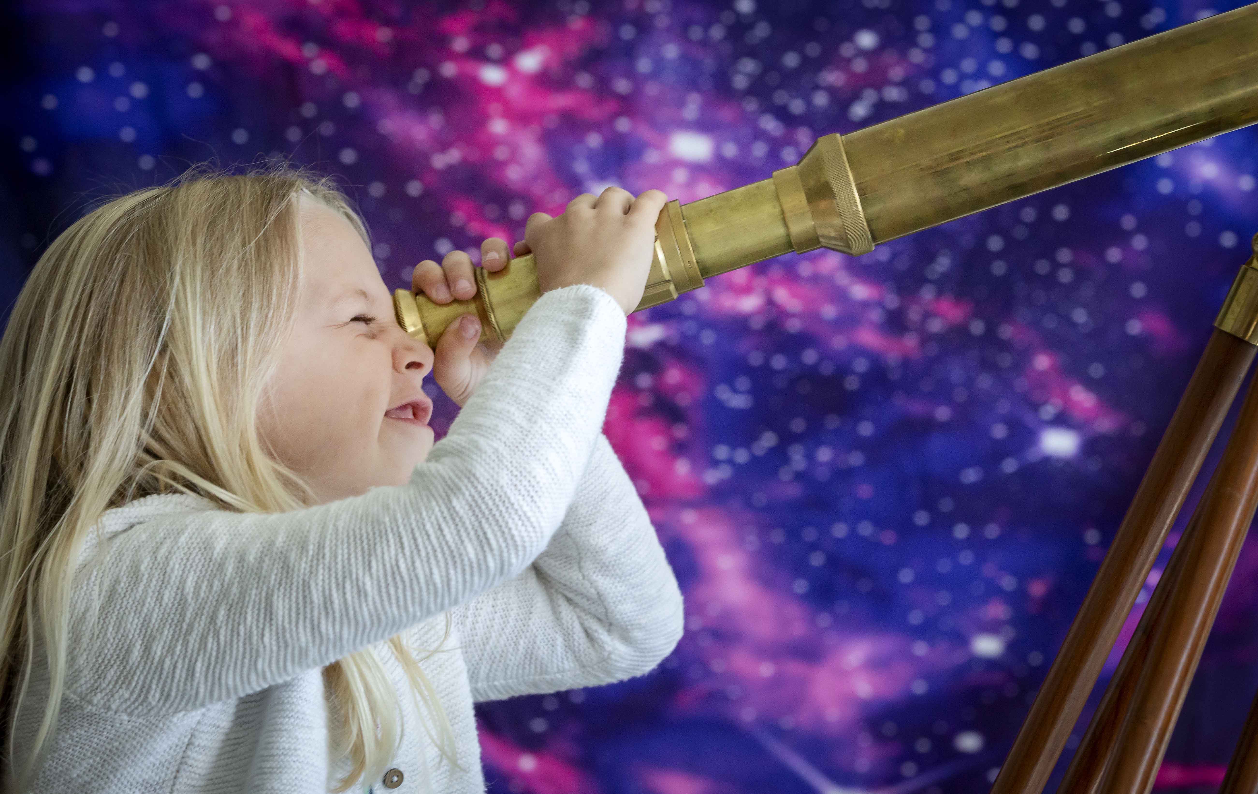 A young girl looks through a telescope. 