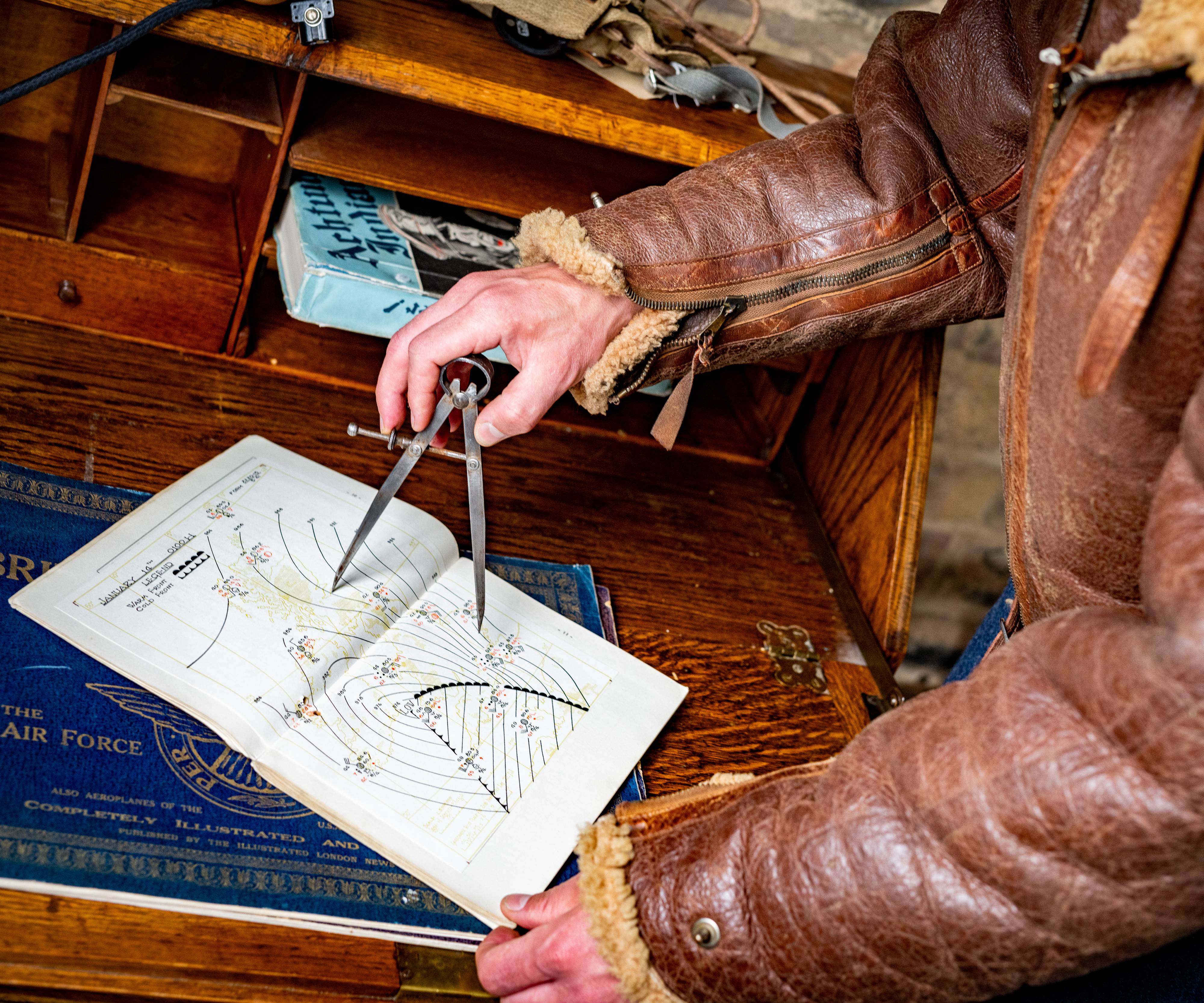 A man wearing an aviator jacket uses a compass on a map of an airfield. 