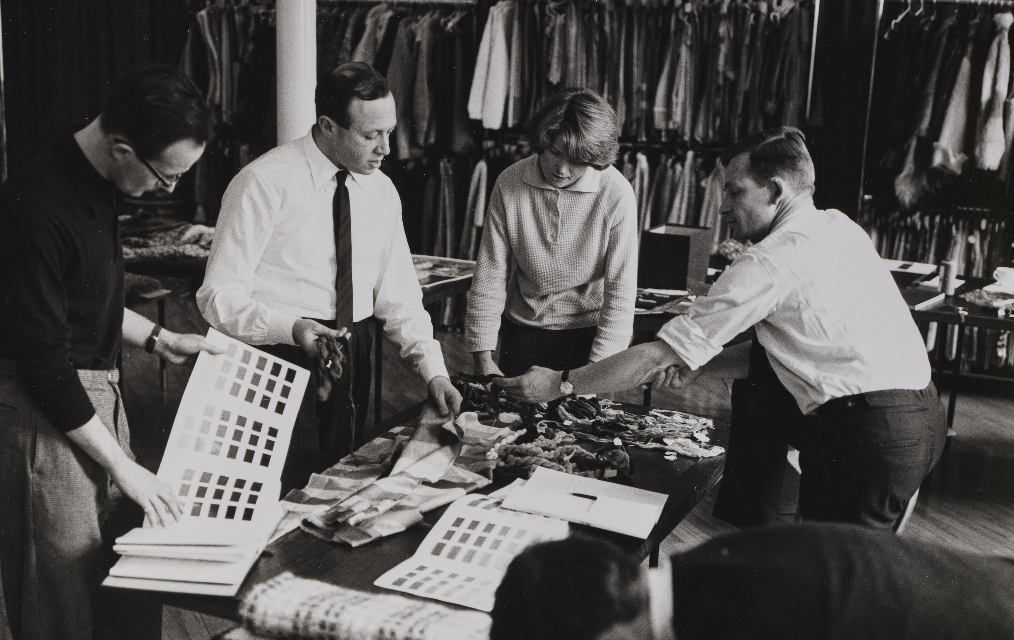 Bernat Klein and colleagues examine swatches of fabric in a black and white photo.