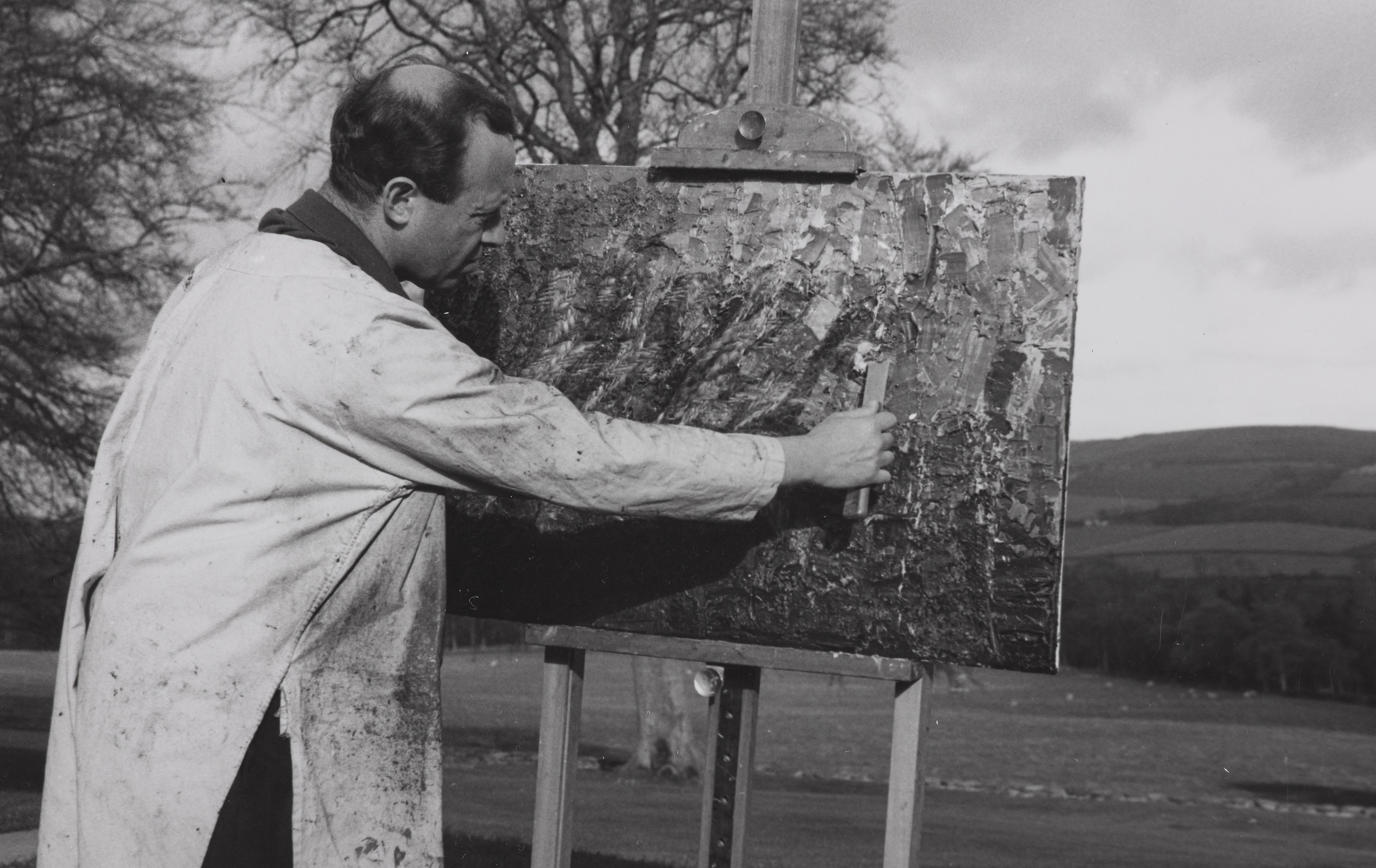 A black and white image of Bernat Klein painting on an easel. 