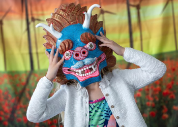 A child holds a blue and brown dragon mask to hide their face. 