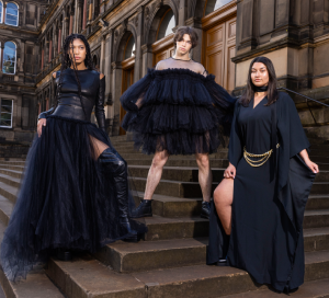 Three models in black attire stand on the steps of National Museum of Scotland. 