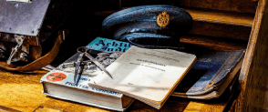 A desk is filled with books and a pilots cap. 