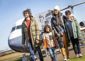 A family walk in front of the BAC 1-11 aircraft outdoors at the National Museum of Flight on a sunny day