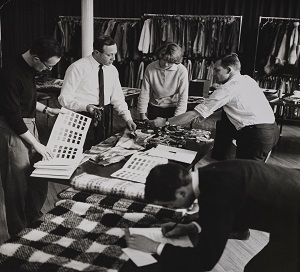 A black and white image of Bernat Klein and his employees looking at fabric samples