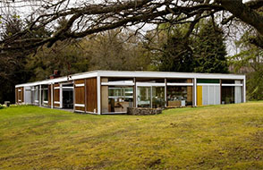 The exterior of High Sutherland, Bernat Klein's modernist home in the Scottish Borders. A one-story building with large glass windows surrounded by trees.