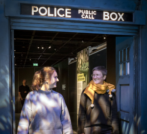 Two people walk through the a doorway styled to look like the TARDIS entrance in the Doctor Who Worlds of Wonder exhibition