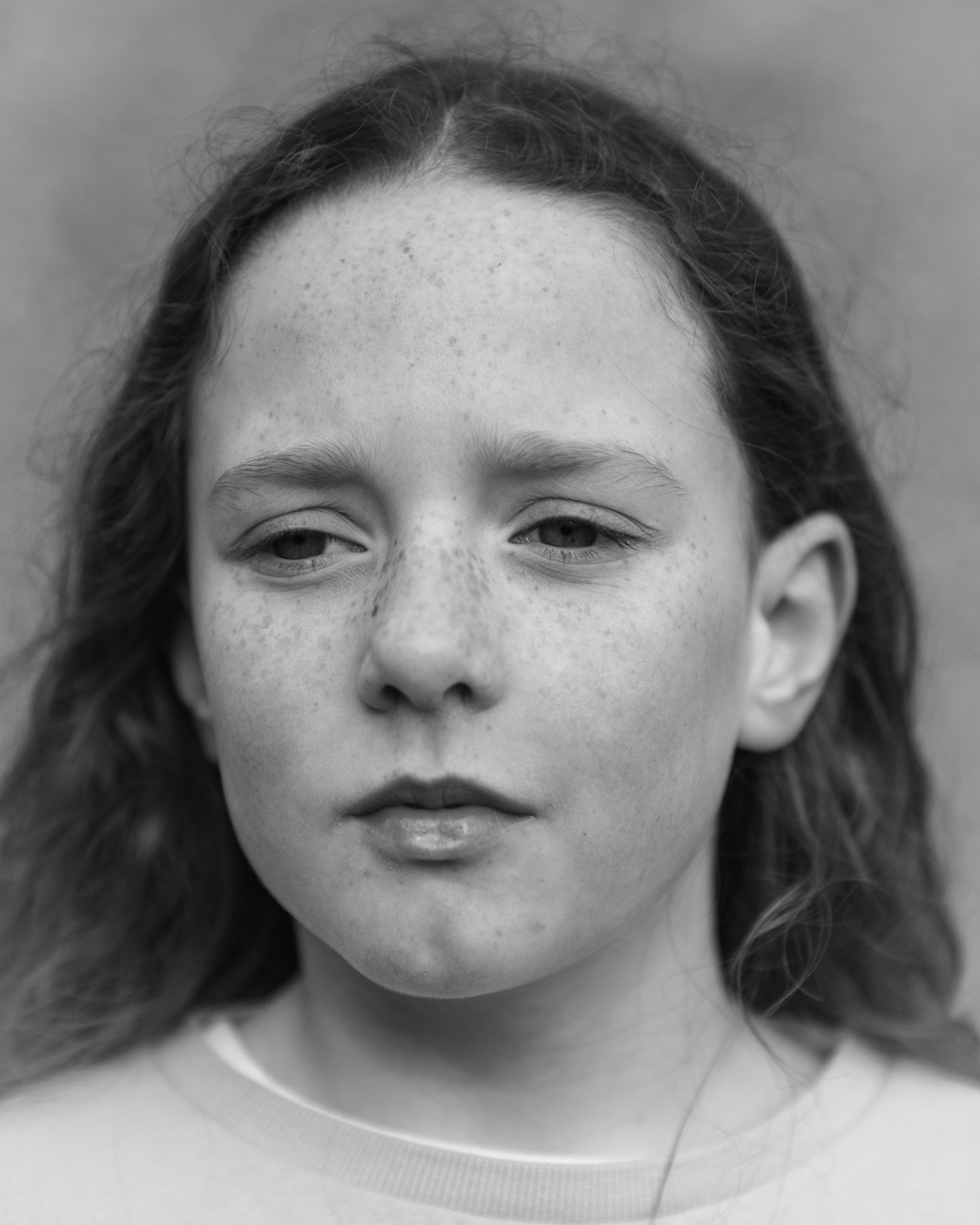 Ein fotografisches Porträt eines jungen weißen Mädchens, das mit einem ernsten Ausdruck an der Kamera vorbeischaut, hat sie gewellte Haare hinter ihrem Ohr versteckt.
