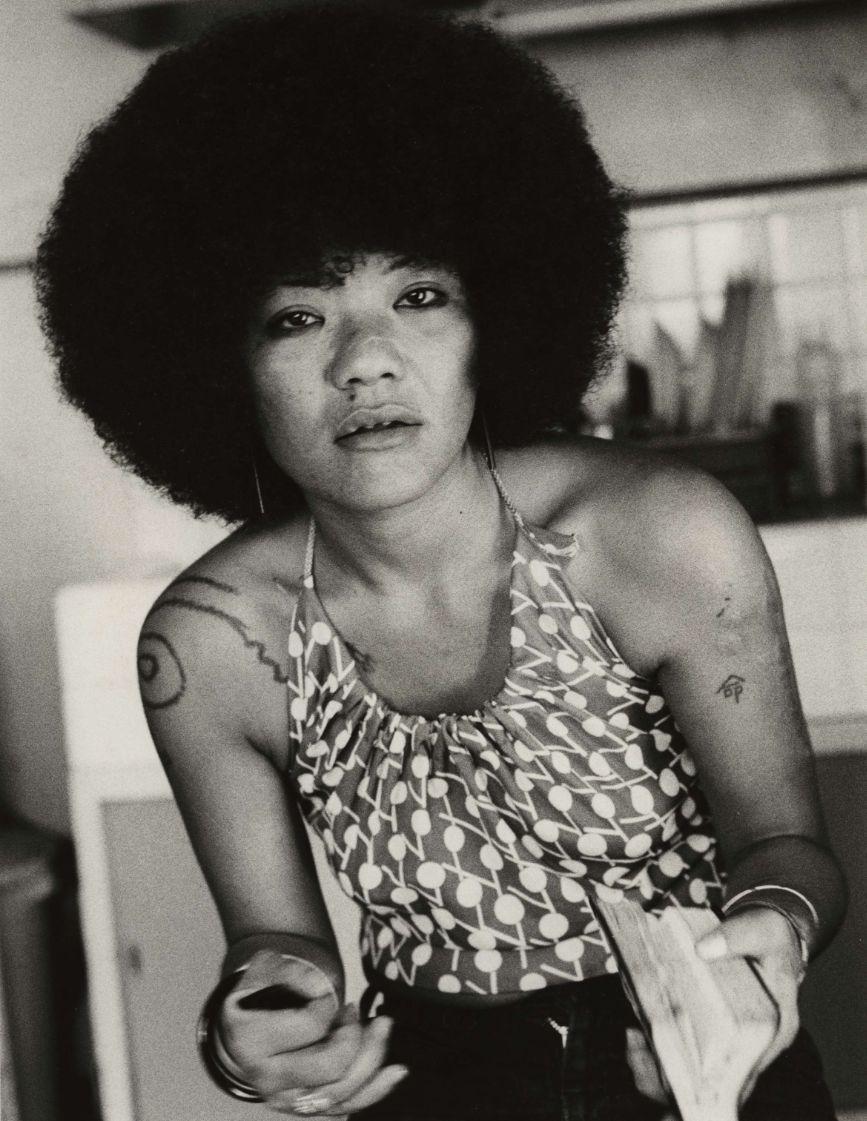 Ein Schwarzweißfoto einer Frau mit Afro, die ein Buch hält. 