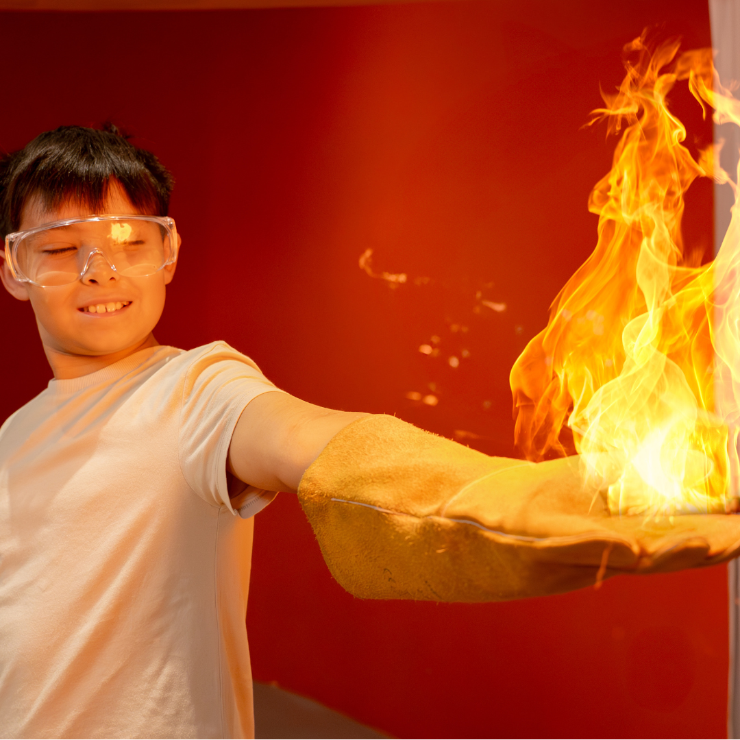 A young boy in a cream t-shirt holding his arm outstretched with a flame on a glove on his hand