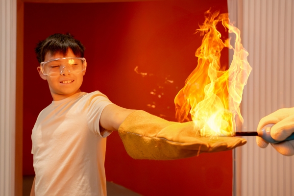 A boy wearing a cream tshirt and heat proof glove with a flame on his hand