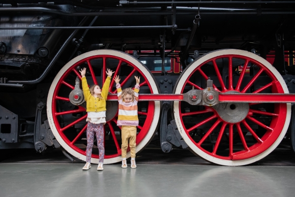 Two girls standing next to a red railway wheel