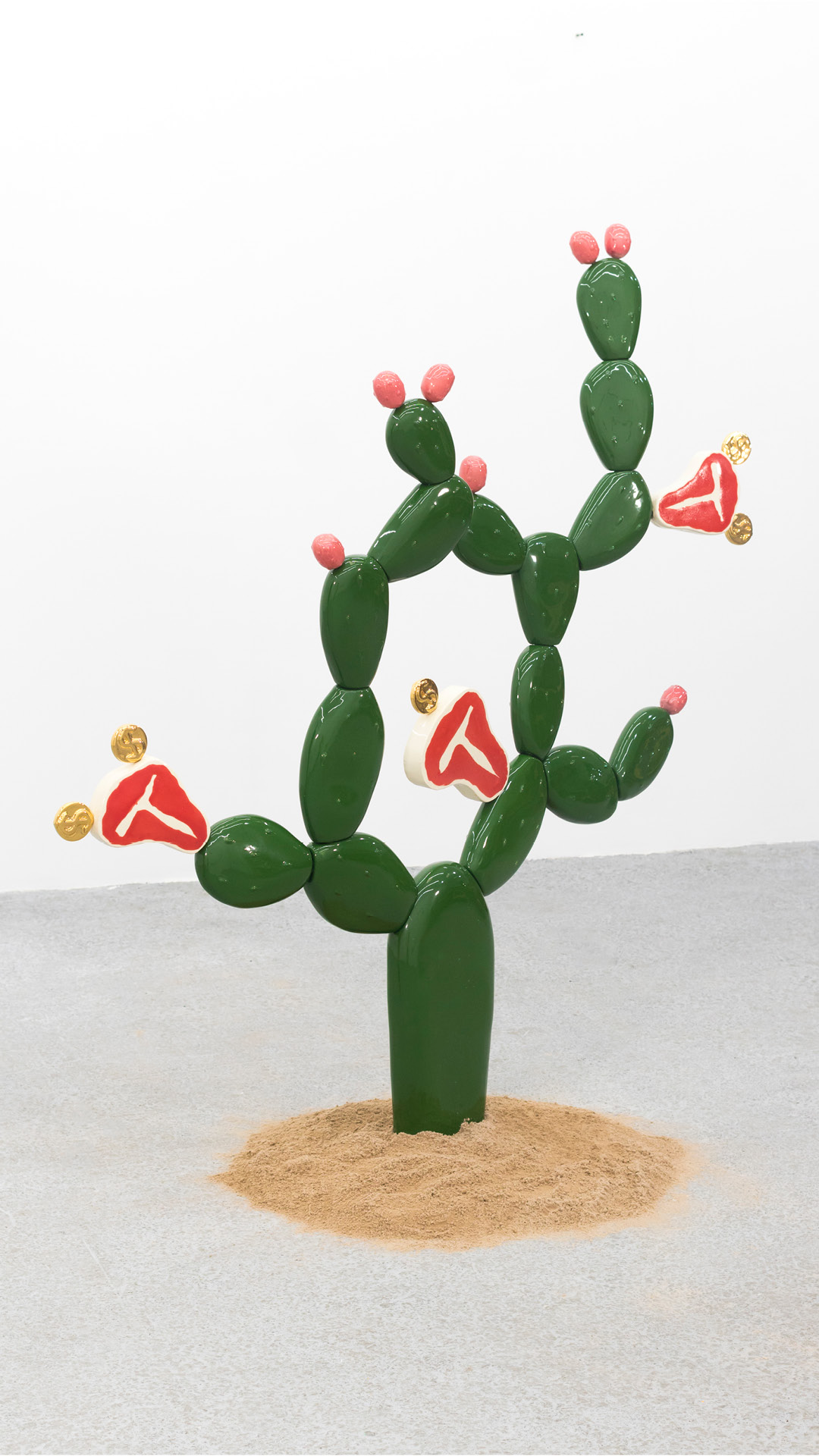 A sculpture of a cactus growing raw steaks and gold coins is displayed in a small pile of sand
