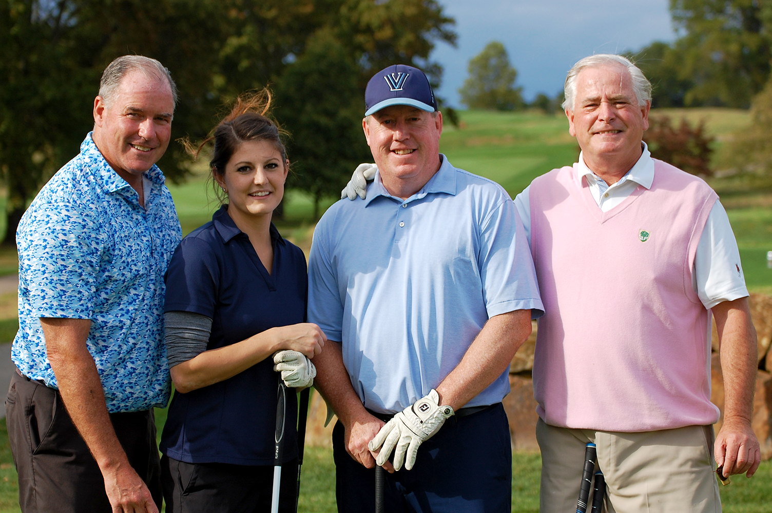 A group of four, three men and a woman, pose for a portrait with their golf clubs at the Golf Classic