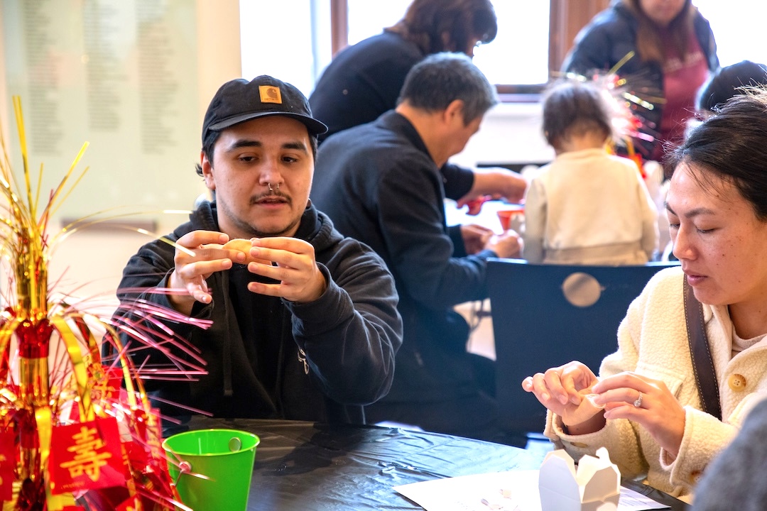 Seated at a table, an art educator demonstrates a project to a museum visitor during a Lunar New Year Community Day.