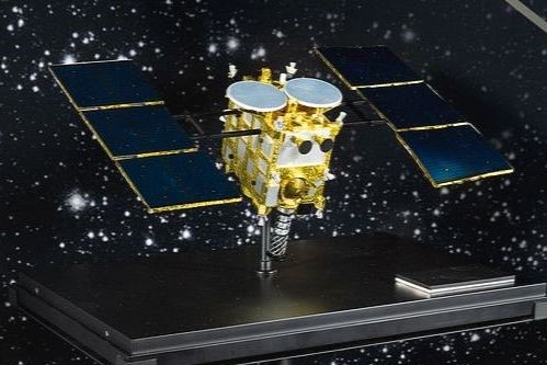 A small object with black panels on either side of a complex gold body. Behind it, a background of stars against dark blue or black. The device has been placed on a black platform.