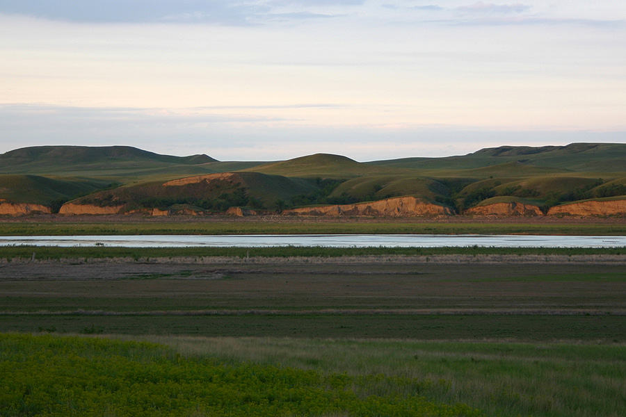 Image of rolling green hillsides with a blue river in front of them, lit at dusk. 