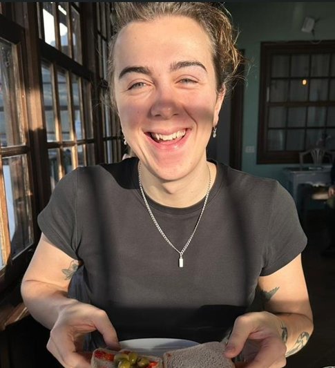 [Image] A photo of HE team member Josiah O'Brien. They are wearing a white t-shirt and smiling.