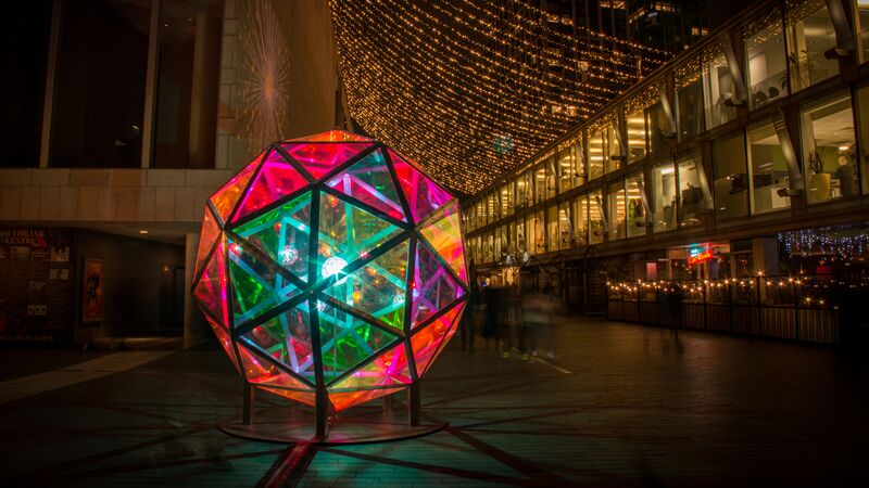 Multicoloured geometric light sculpture made of triangles into a large dome outside a row of lit buildings