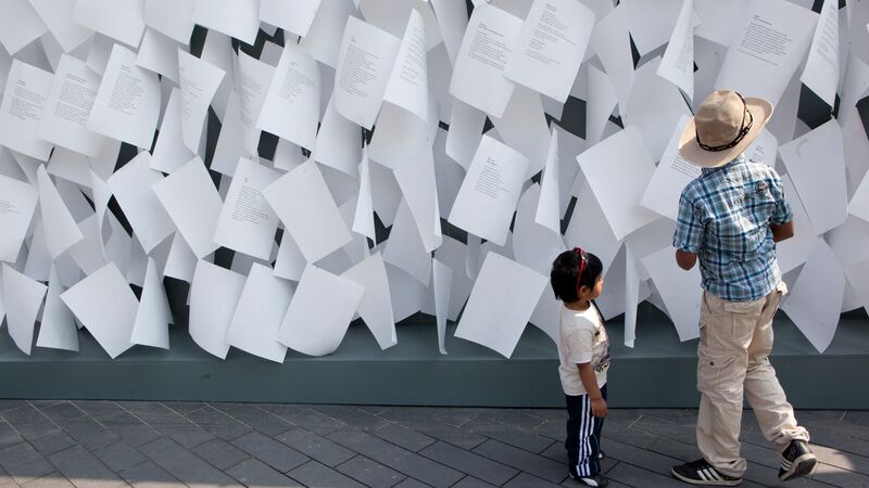 Pages of paper on a wall with two children in front.