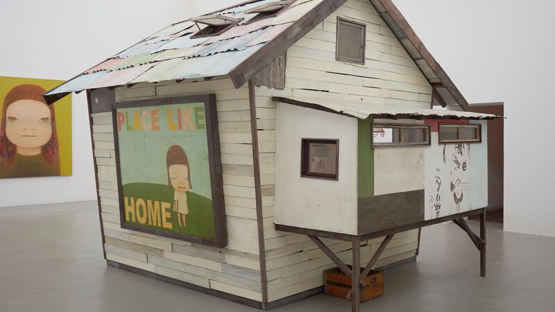 House sculpture inside a white gallery space with the words 'place like home' with a small figure painted on the side