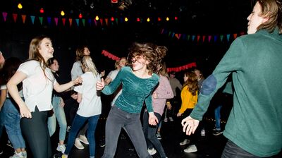 Group of young people dancing in a dark room with bunting and fairy lights, they are smiling and talking