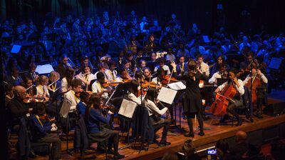 Children on an auditorium stage performing using orchestral instruments. 
