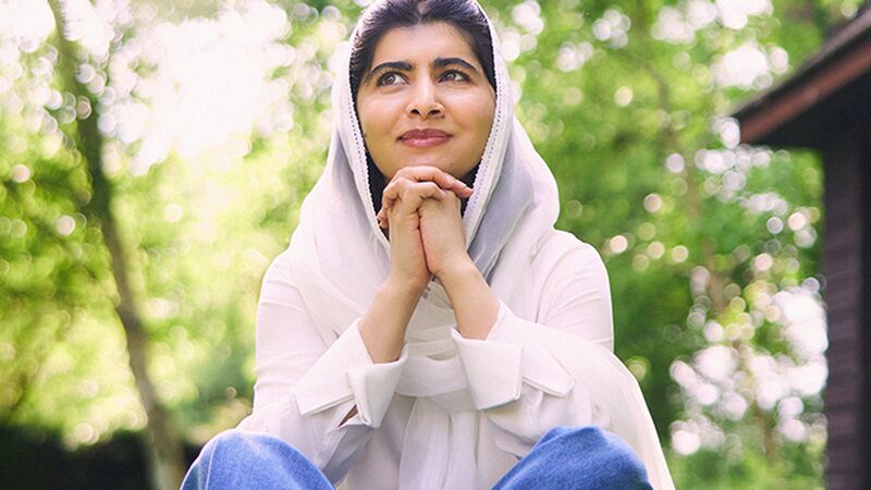 Malala wearing a white top sat in a wooded area