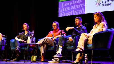 A panel discussion featuring four speakers seated in blue chairs, engaged in conversation.