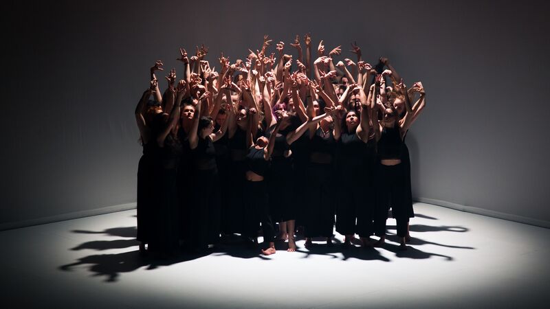 Dancers wearing black on stage all lifting their arms upwards