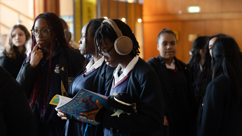 A student stood reading a Southbank Centre event guide amongst a group in the Royal Festival Hall