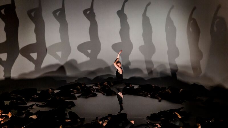 Dancers wearing black laying down on stage with one dancer standing and lifting their arm upwards