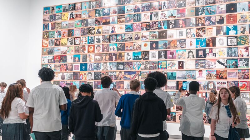 A group of students stood facing a large-scale artwork in the Hayward Gallery made up of various small photos