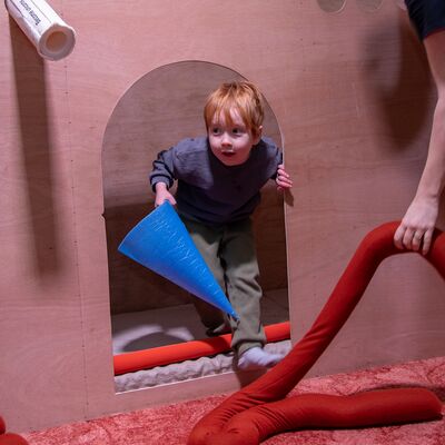 A little child with ginger hair is peeking through an installation in Replay.