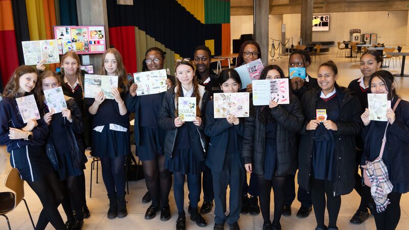 A group of students holding up zines inside of the Queen Elizabeth Hall