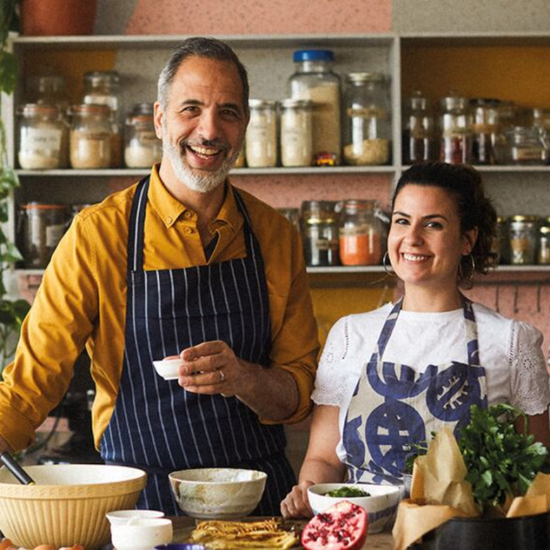 Yotam Ottolenghi on the left holding bowl & Noor Murad on the right. Seen on their cookery set with apron