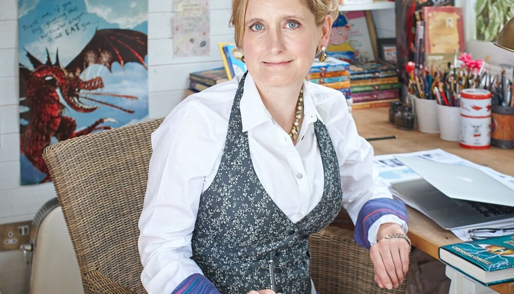 Author Cressida Cowell sits with a pencil in her hand in front of her "How to Train Your Dragon" illustrations.
