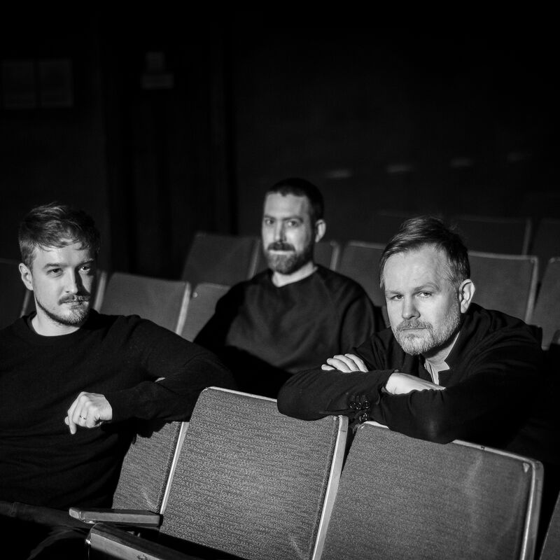 Musicians Daniel Pioro, Valgeir Sigurðsson & Liam Byrne in a dark auditorium
