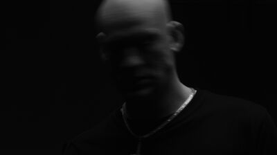 A blurry black and white image of an person in movement. They wear a cross on a silver chain