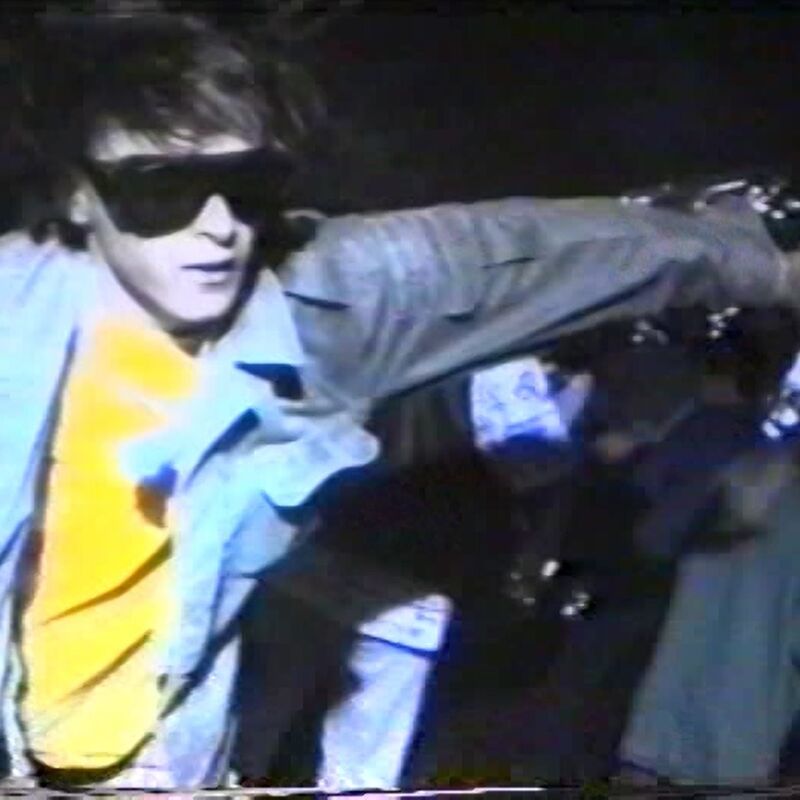A clip from a short film featuring a man wearing big sunglasses, a denim jacket and a bright orange tshirt