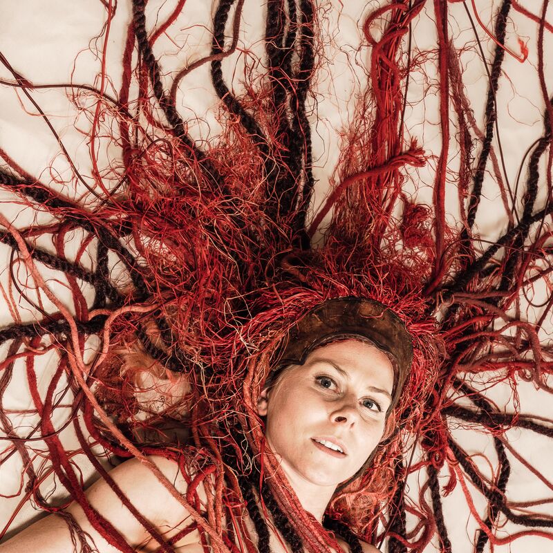 White woman lies on the floor with red braids fanned around her head.