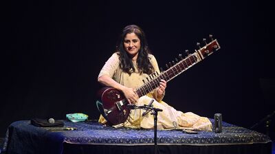 Sitar player Roopa Panesar sat playing her instrument in a cream outfit.