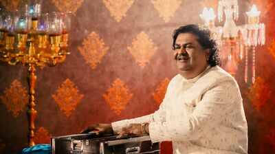 Artist Osman Mir sat next to a harmonium.