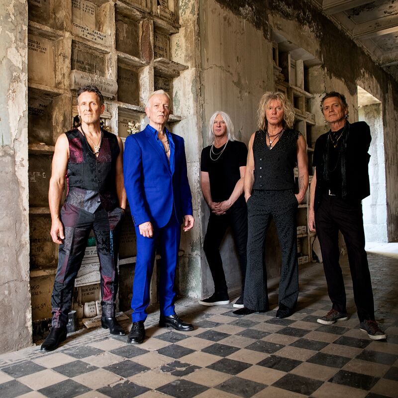 The 5 members of Def Leppard pose in a once grand but now dilapidated corridor, looking older but still 100% rock'n'roll