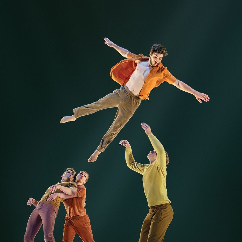 Four Circa acrobats performing, with three standing and looking up at the 4th who is in the air