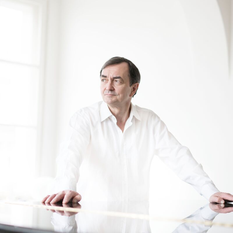 Pianist Pierre-Laurent Aimard dressed in white standing by a white piano