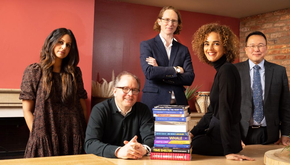 the 5 International Booker prize judges sit together around desk which has the longlist of books atop it  